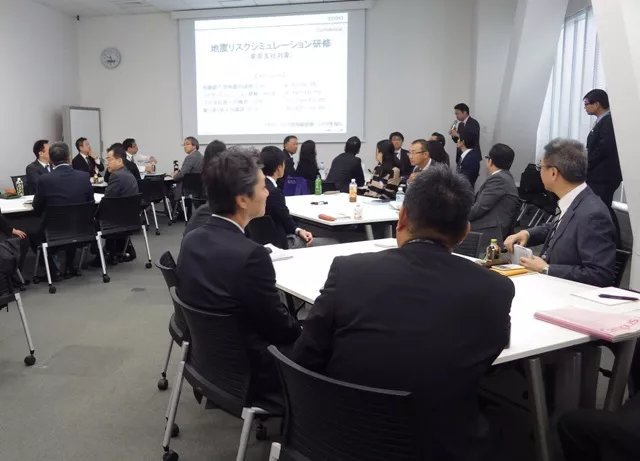 In a conference room, employees are conducting risk simulations while looking at a screen.
